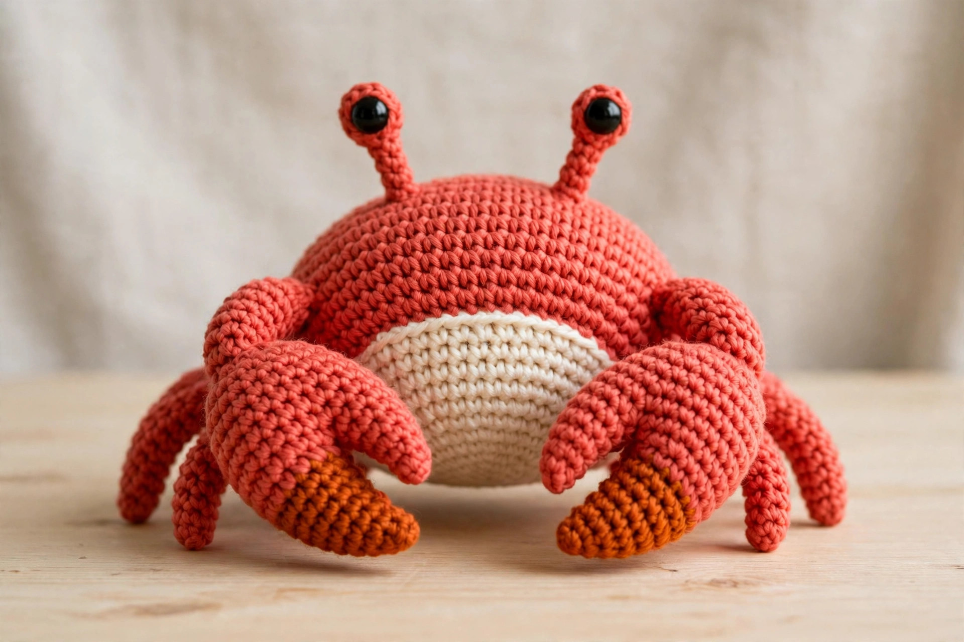 Front view of a coral red crochet crab with cream belly, black eyes on stalks and big orange-tipped claws