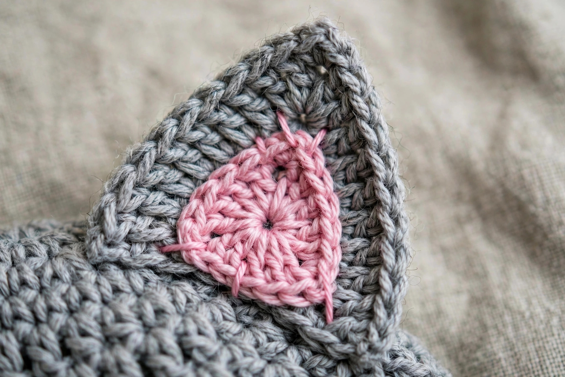 Close-up of the pink inner ear stitched onto the gray outer ear of a crocheted cat beanie
