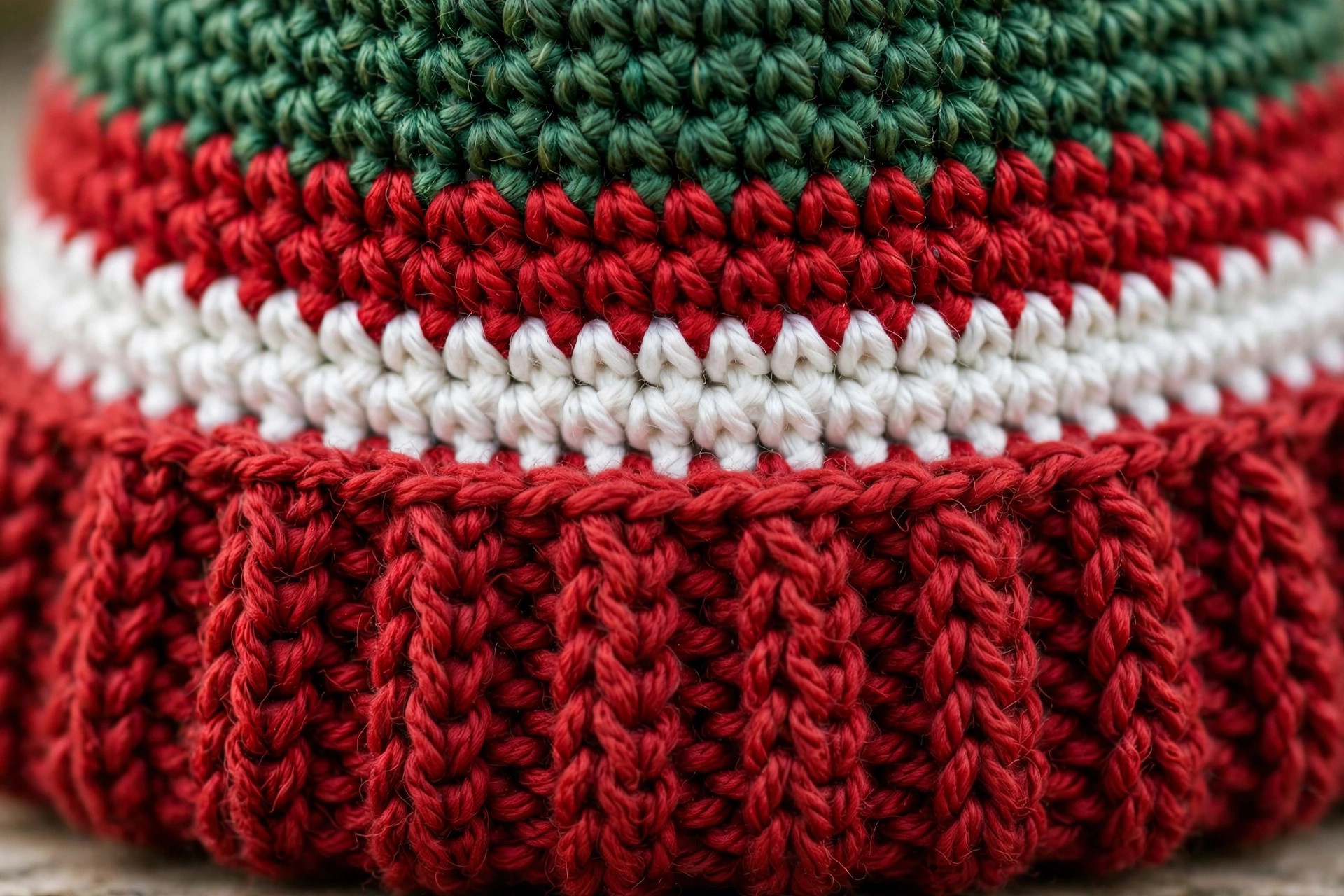 Close-up of the red ribbed post-stitch brim and a red and white stripe band on a green crochet elf hat