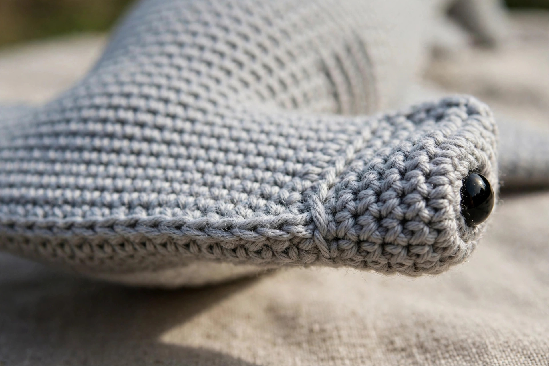 Close-up of a crochet hammerhead shark hammer head showing tight grey stitches and a safety eye at the end of the hammer