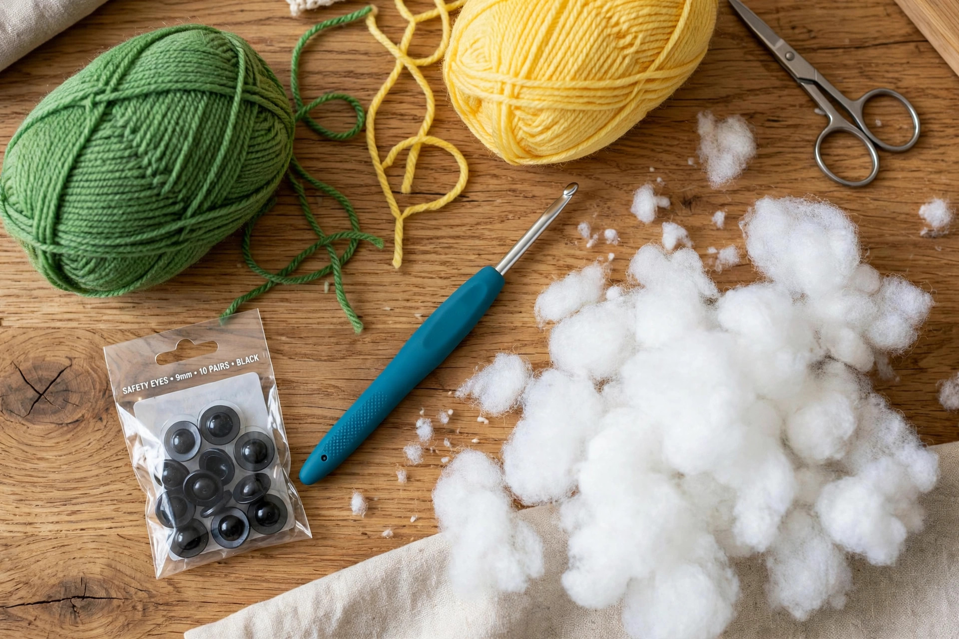 Materials flat lay for a crochet lizard pattern: green and yellow yarn balls, black safety eyes, a crochet hook and white stuffing on a wooden table