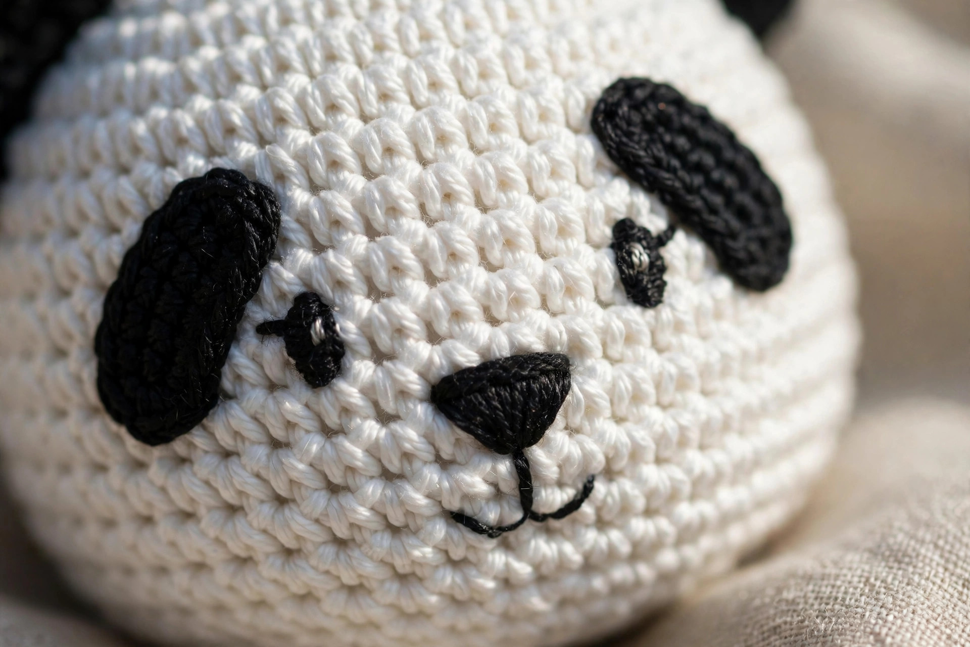 Close-up of the crochet panda's face showing black eye patches, embroidered eyes, nose and smile