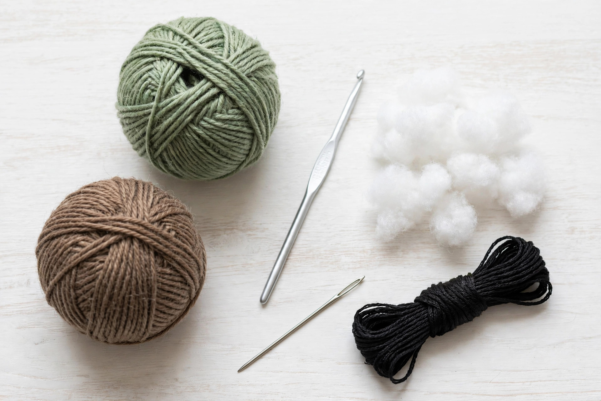 Flat lay of green and brown yarn balls, a crochet hook, white toy stuffing, black embroidery floss and a tapestry needle for making the crochet pickle pattern free