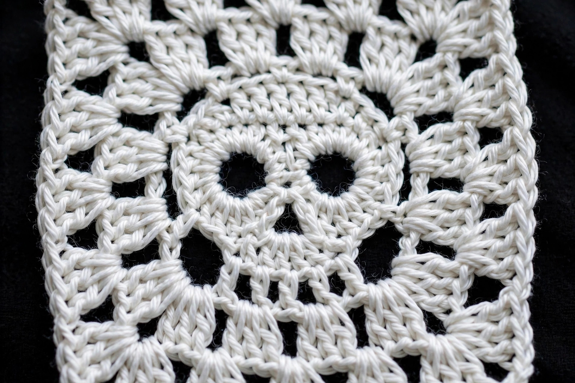 Close-up of one crochet skull motif square showing white skull, black eye discs and charcoal background stitches