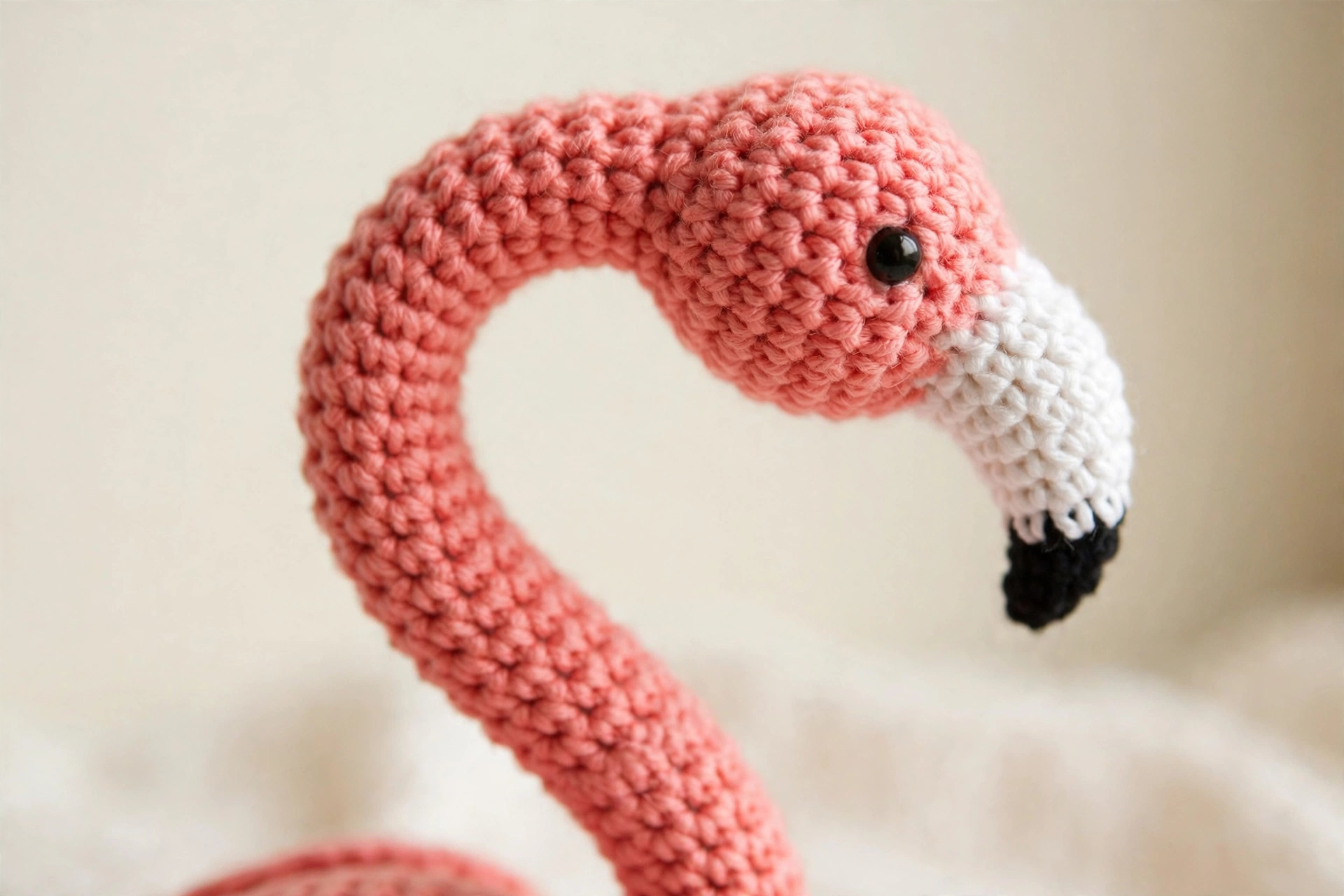 Close-up of the crochet flamingo head and neck showing the curved white beak with black tip and pink single-crochet texture