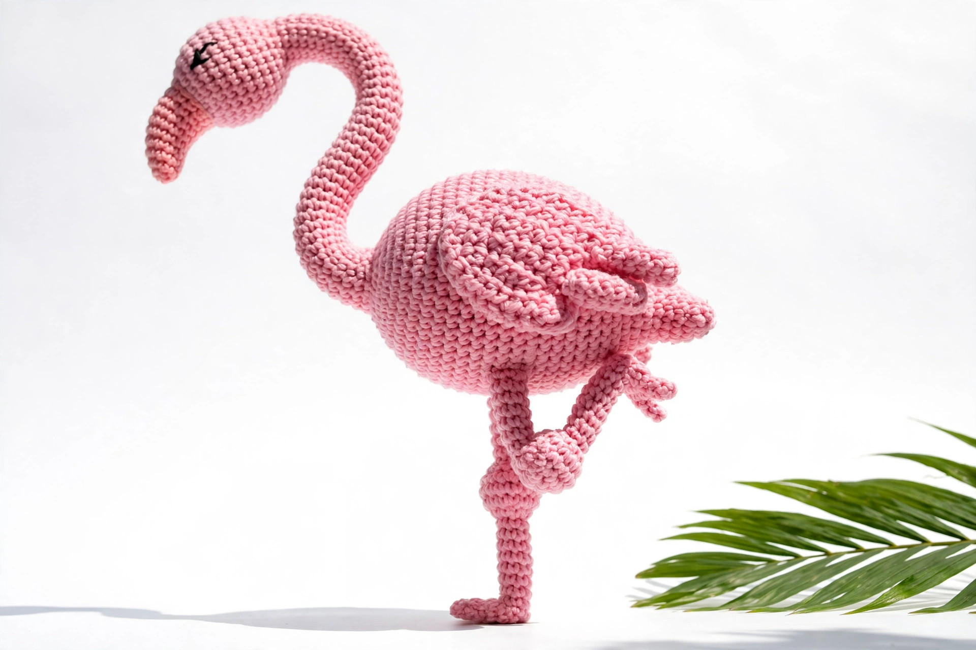 Pink crochet flamingo standing on one long skinny leg with the other leg tucked up, showing the balanced one-leg pose