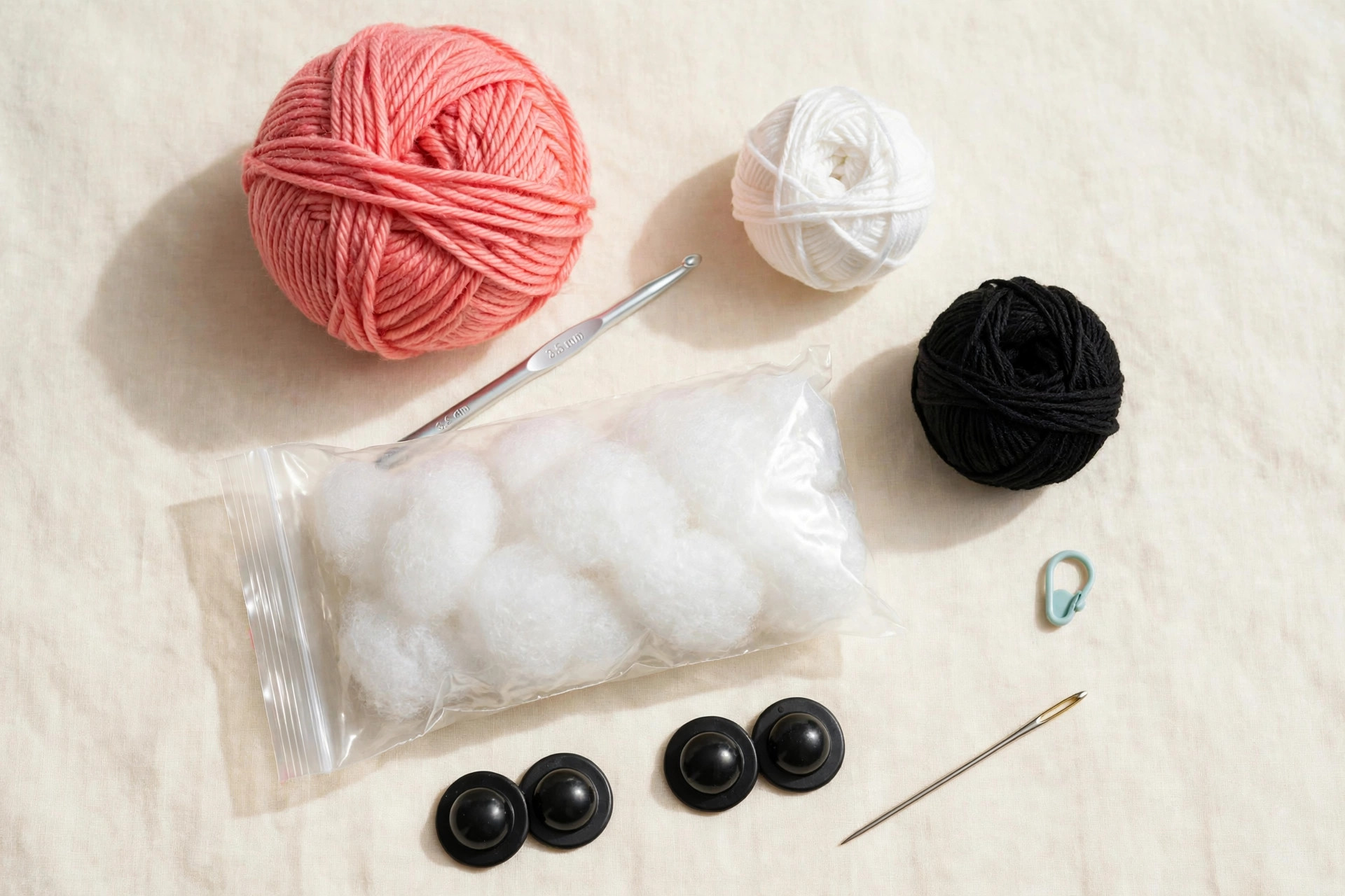 Crochet materials flat lay for the flamingo pattern: coral pink yarn, white and black yarn, 3.5 mm hook, fiberfill, safety eyes, yarn needle and stitch marker