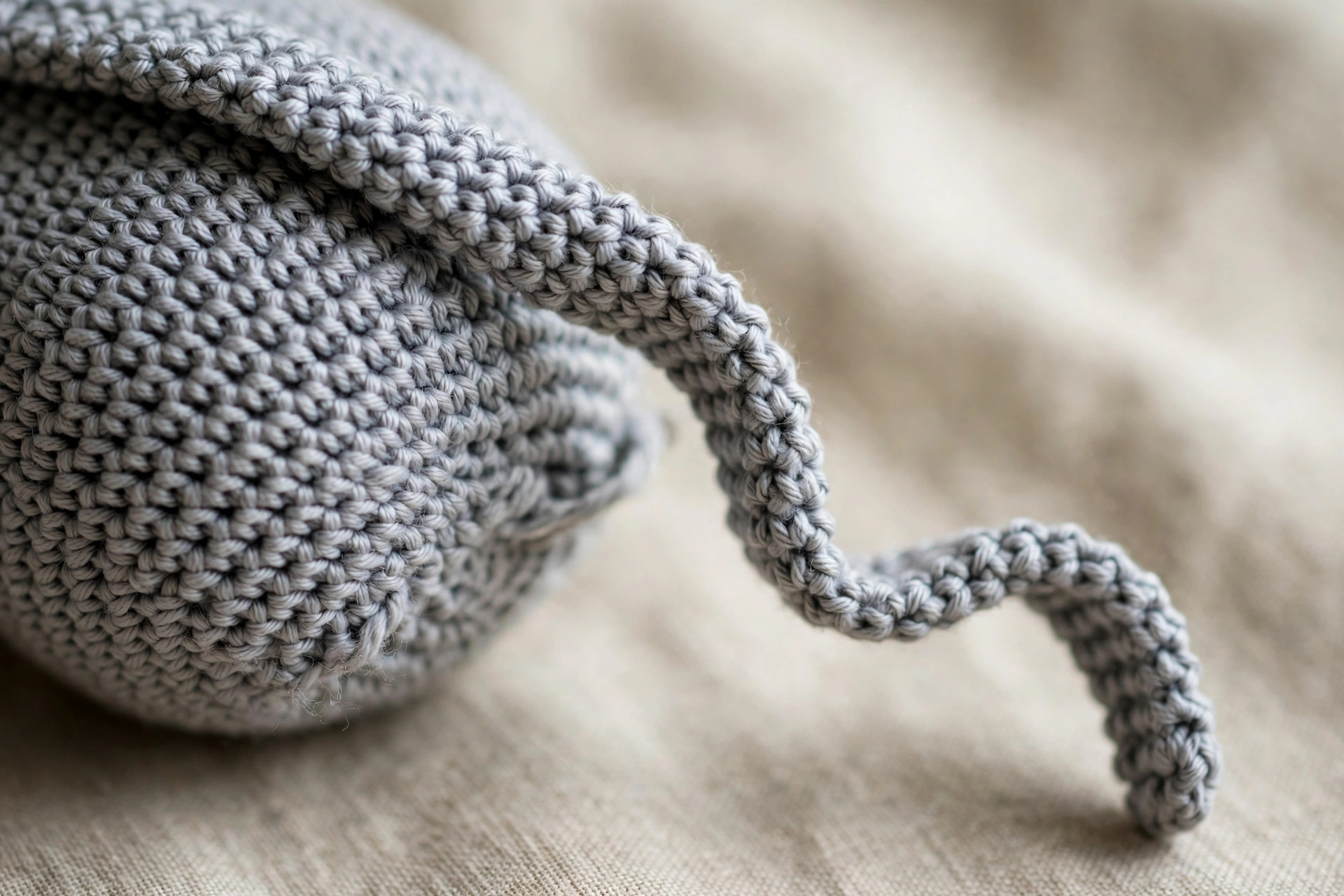 Close-up of neat single-crochet stitches in grey yarn with a long thin lightly-stuffed floppy cat leg stretching across the frame