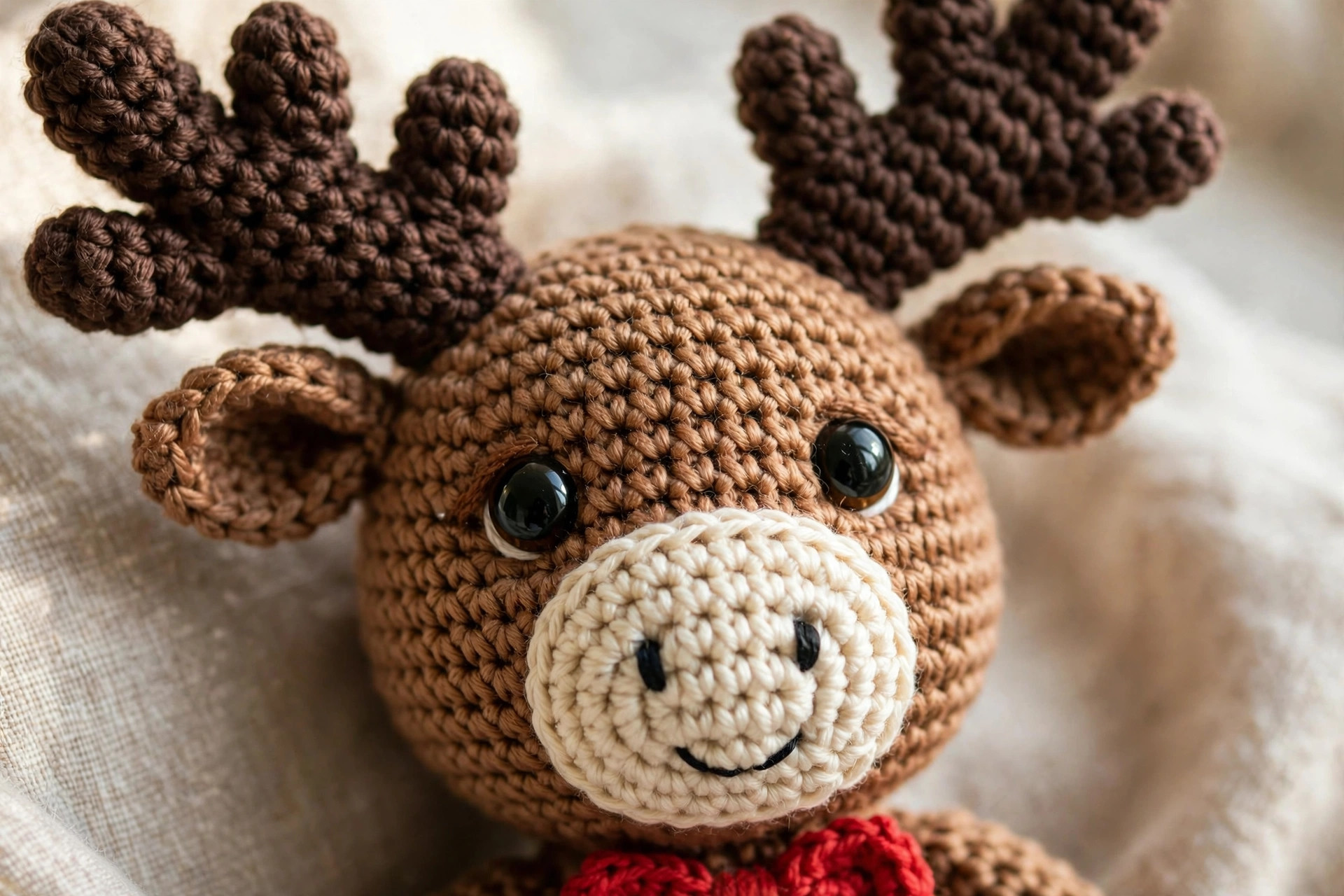 Close-up of a crochet moose head showing the cream muzzle, black safety eyes, dark brown antlers and red bow tie