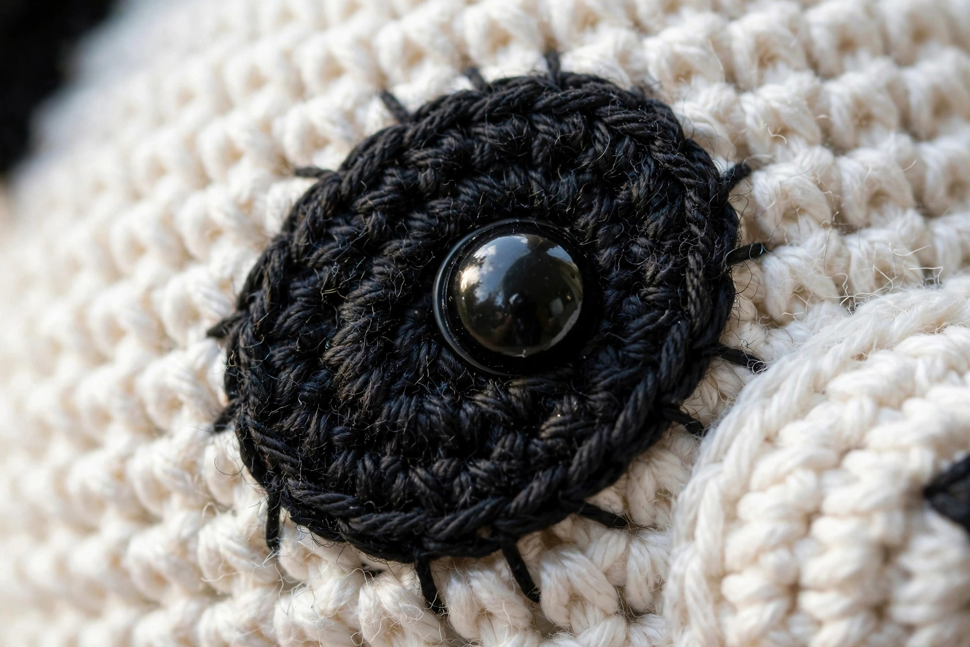 Close-up of the black oval eye patch stitches and safety eye on a handmade crocheted amigurumi panda head, free crochet panda pattern
