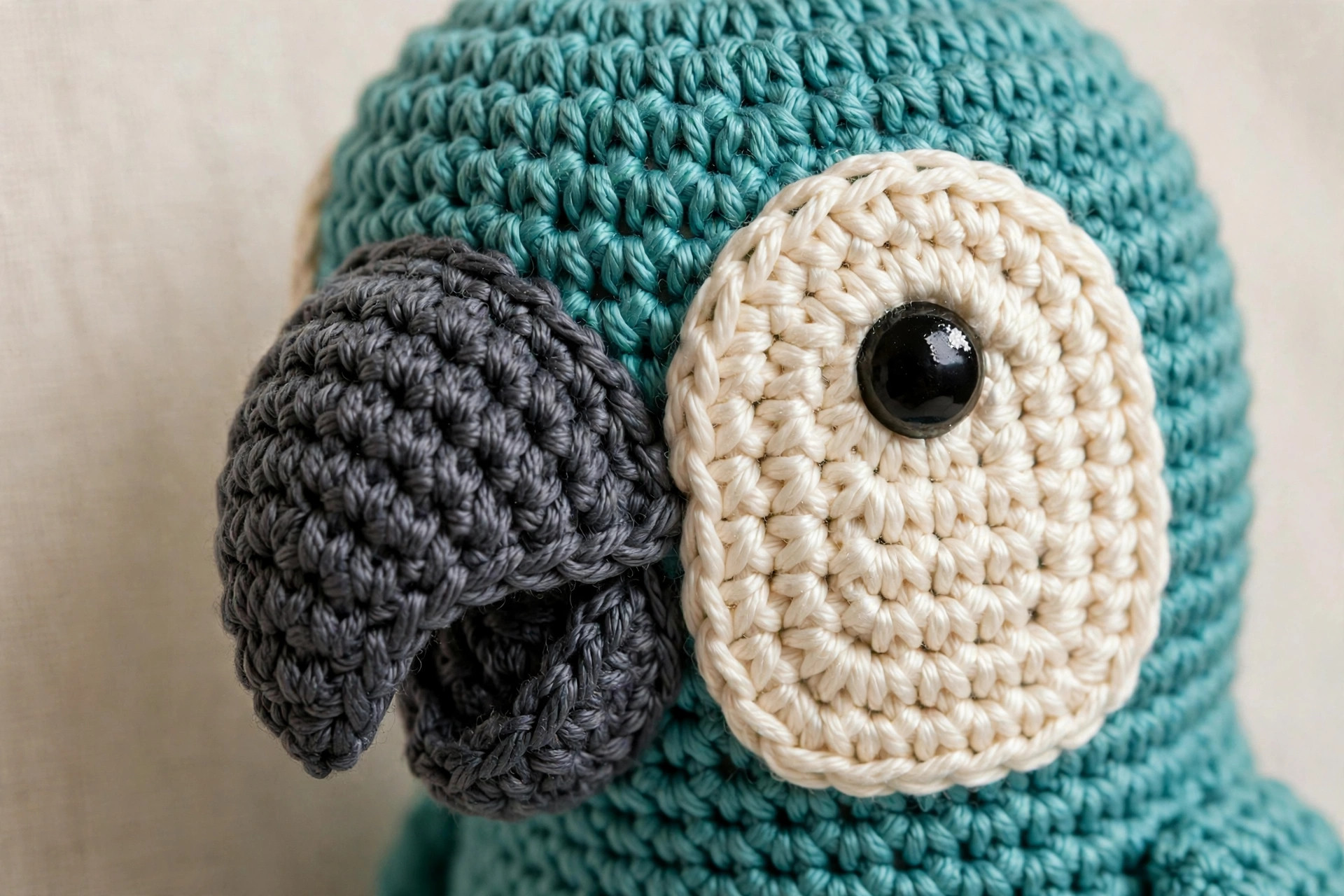 Close-up of crochet parrot face showing two-piece curved grey beak, cream face patch and black safety eye