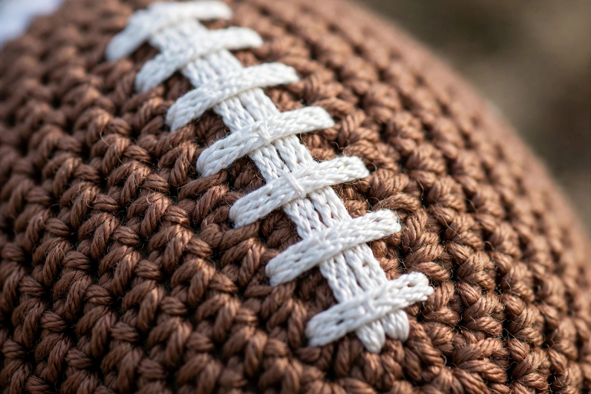 Close-up of embroidered white laces and neat single crochet stitches on a brown crocheted football, crochet football pattern detail