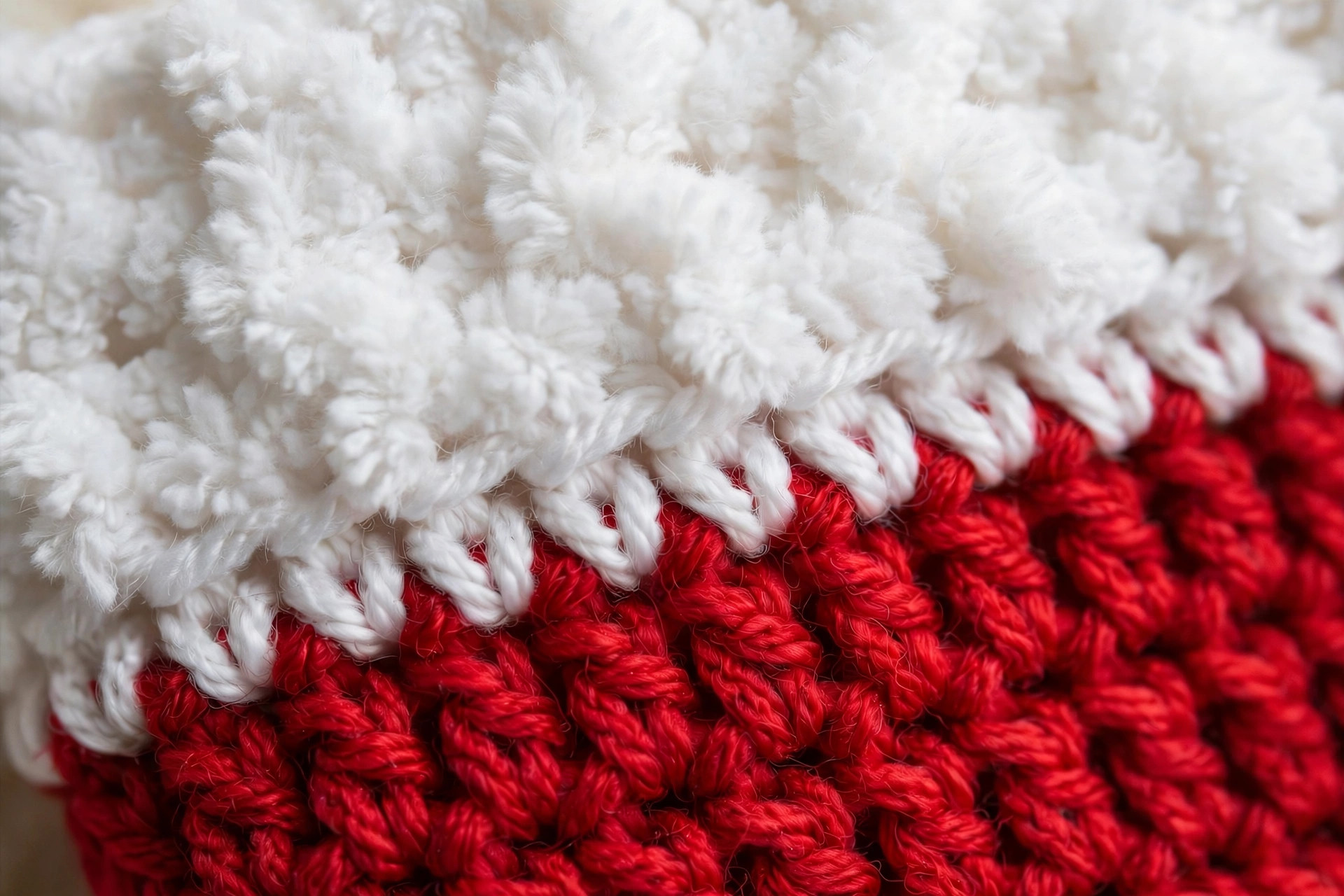 Close-up detail of the fluffy white brim stitches and the join between the white brim and the red body of a handmade crocheted Santa hat, free crochet Santa hat pattern