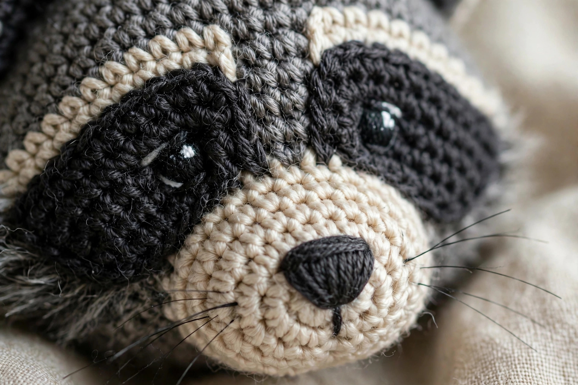 Close-up detail of a handmade crocheted raccoon face showing the black bandit mask, embroidered eyes and stitched nose, free raccoon crochet pattern