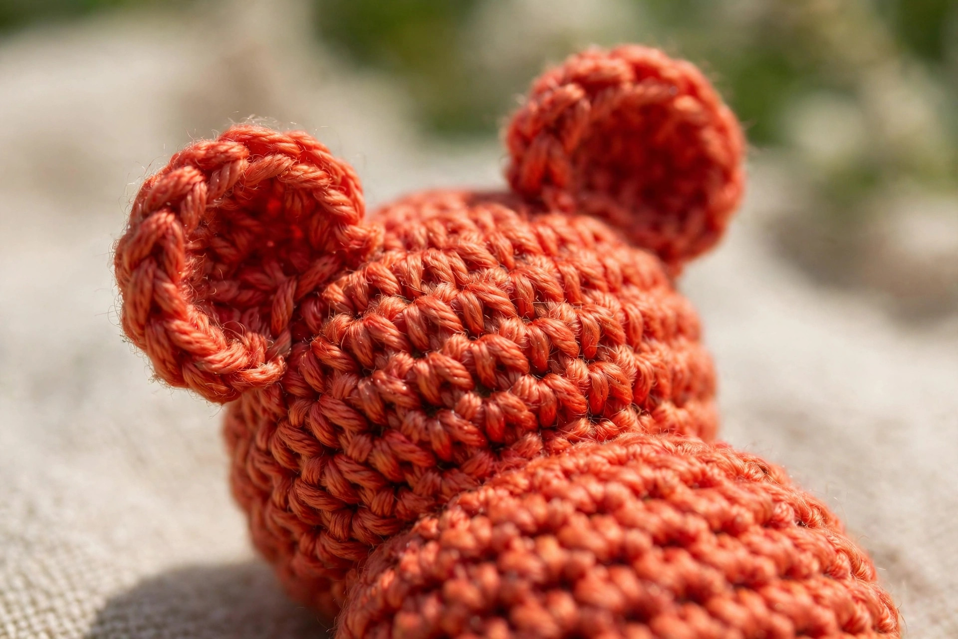 Close-up detail of the crochet stitches and little rounded ears on a handmade red-orange crocheted gummy bear, showing neat amigurumi fabric, gummy bear crochet pattern