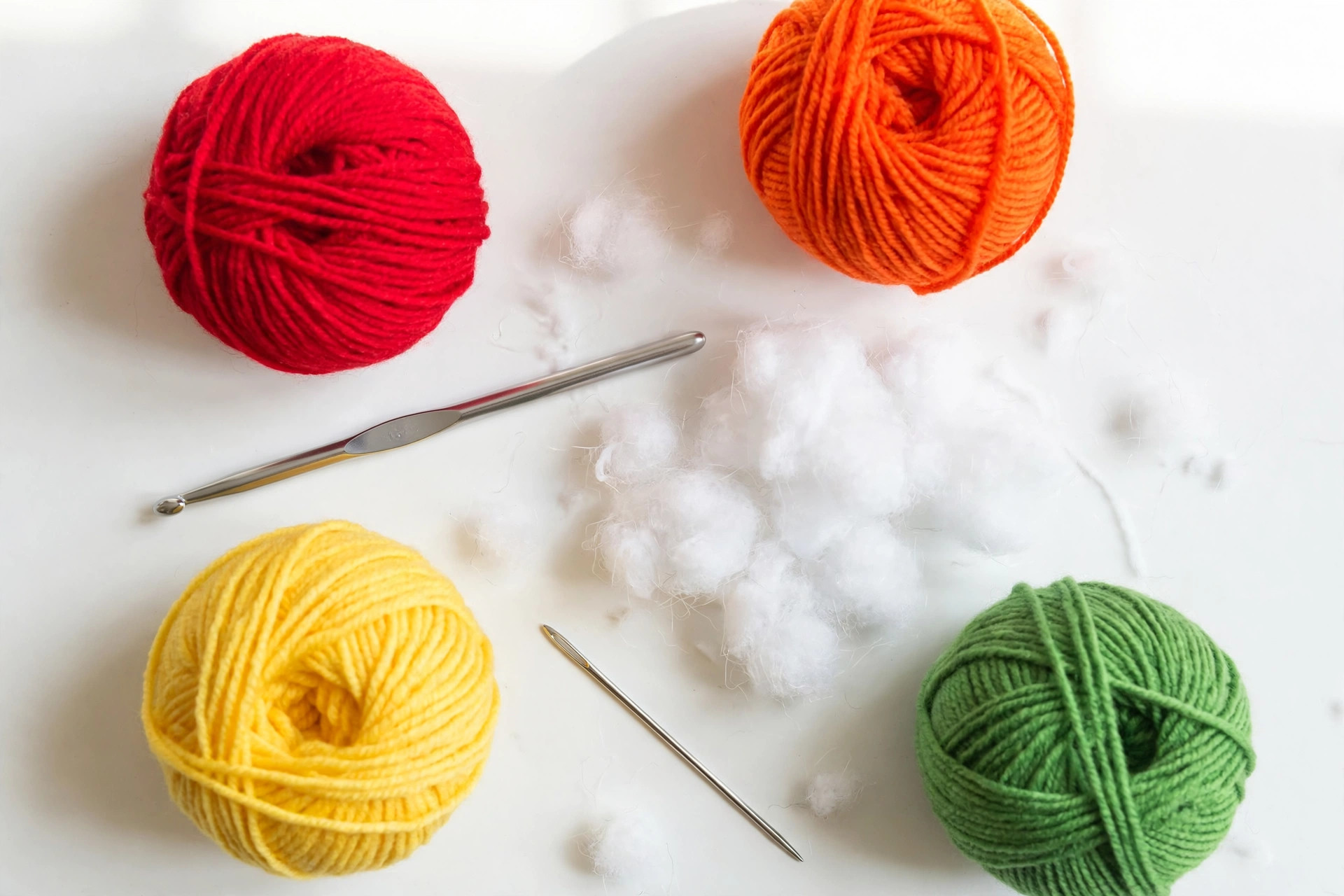 Flat lay of colorful yarn balls, a crochet hook, white toy stuffing and a tapestry needle for making the gummy bear crochet pattern