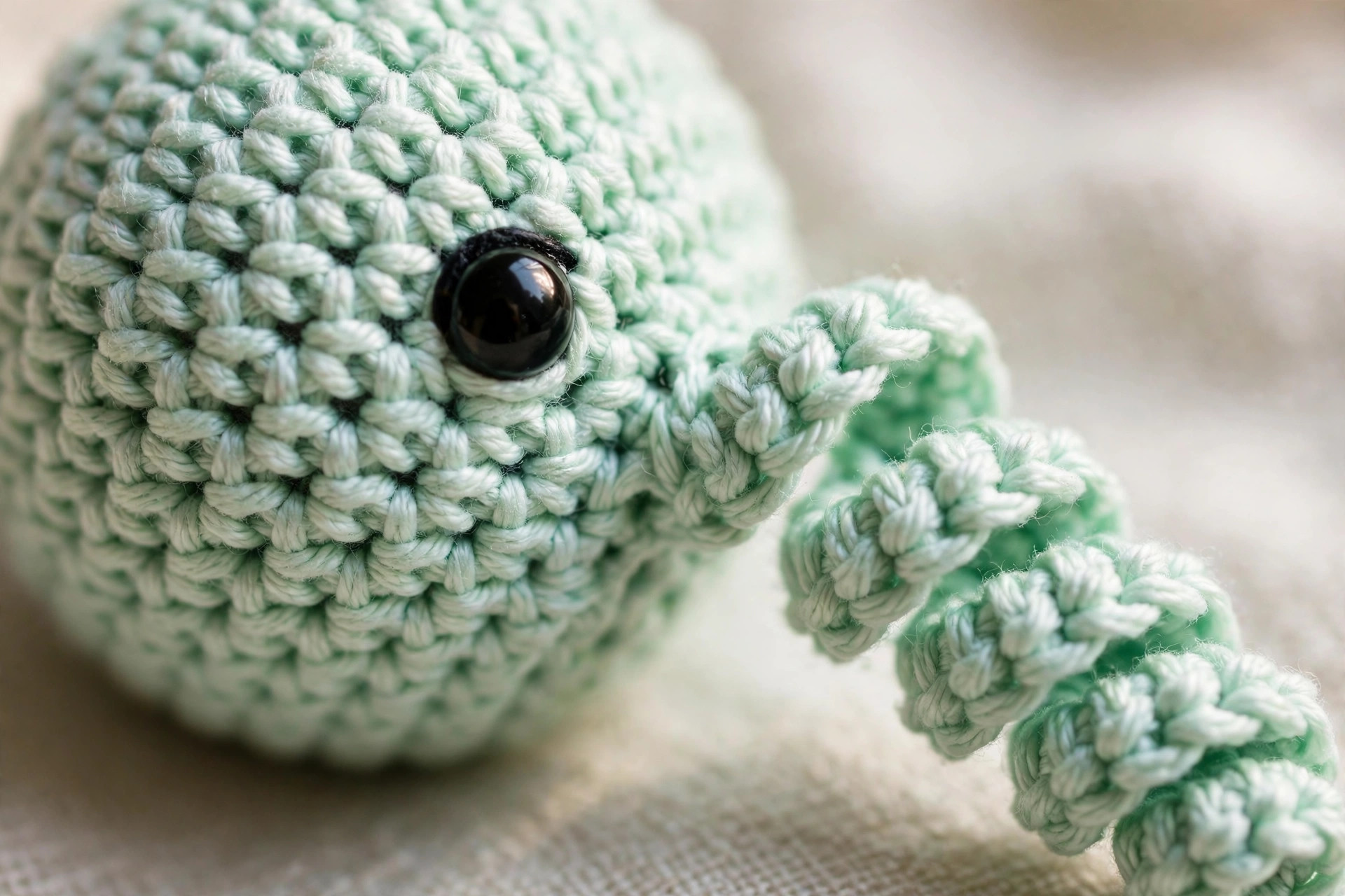 Close-up of neat single crochet stitches, a black safety eye and a curly tentacle on a tiny handmade crochet octopus, mini octopus crochet pattern