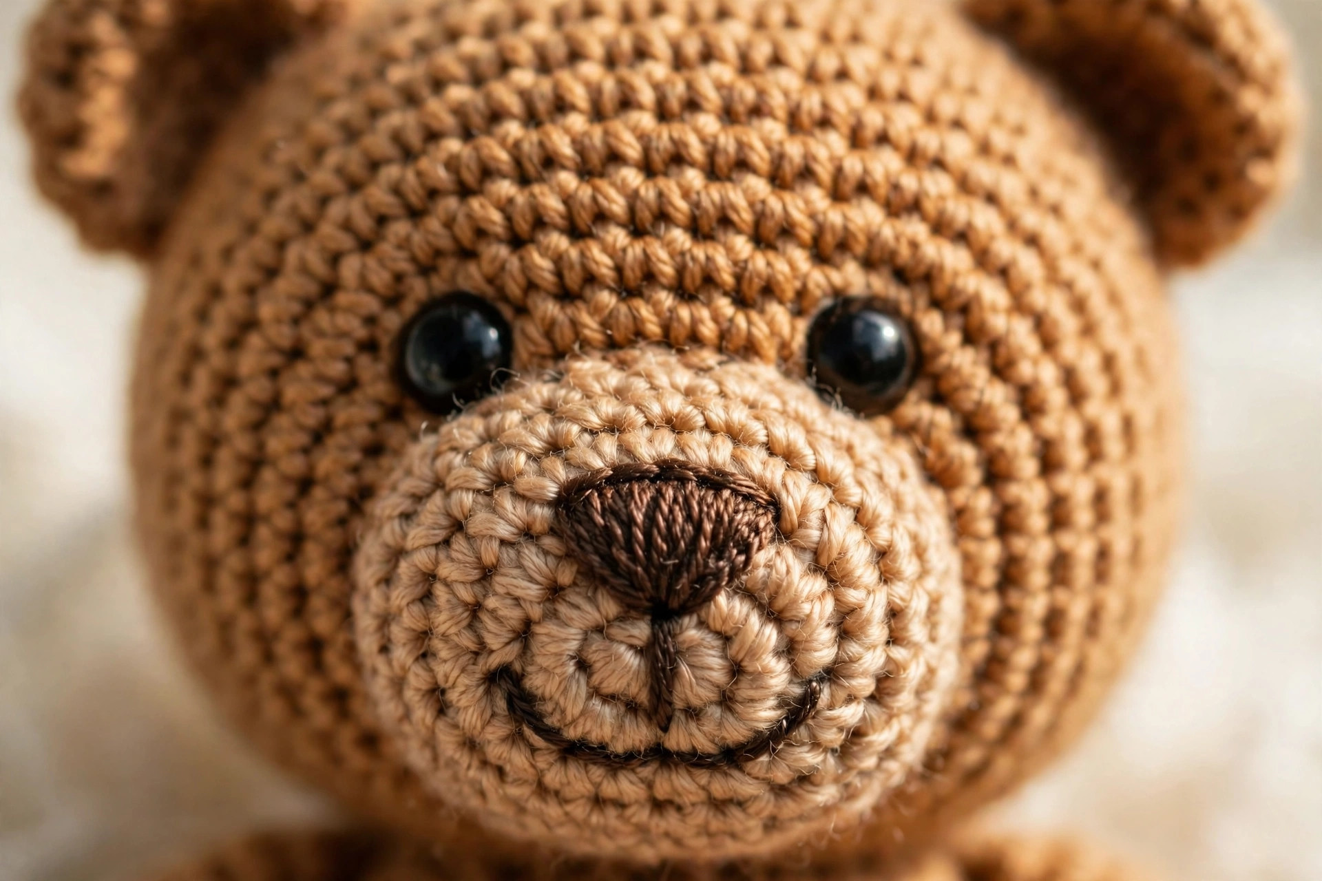Close-up of a one piece crochet teddy bear face showing embroidered nose, mouth and glossy eyes