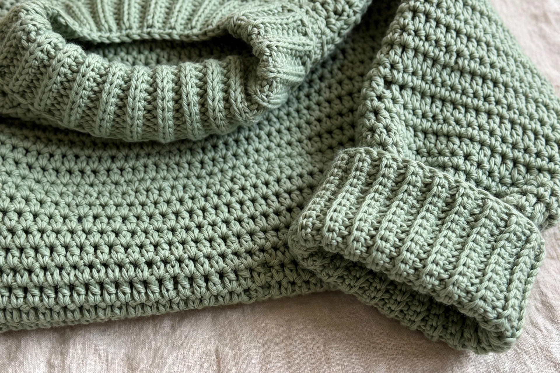 Close-up of a ribbed crochet sleeve cuff and neckband on an oversized sweater in sage green yarn
