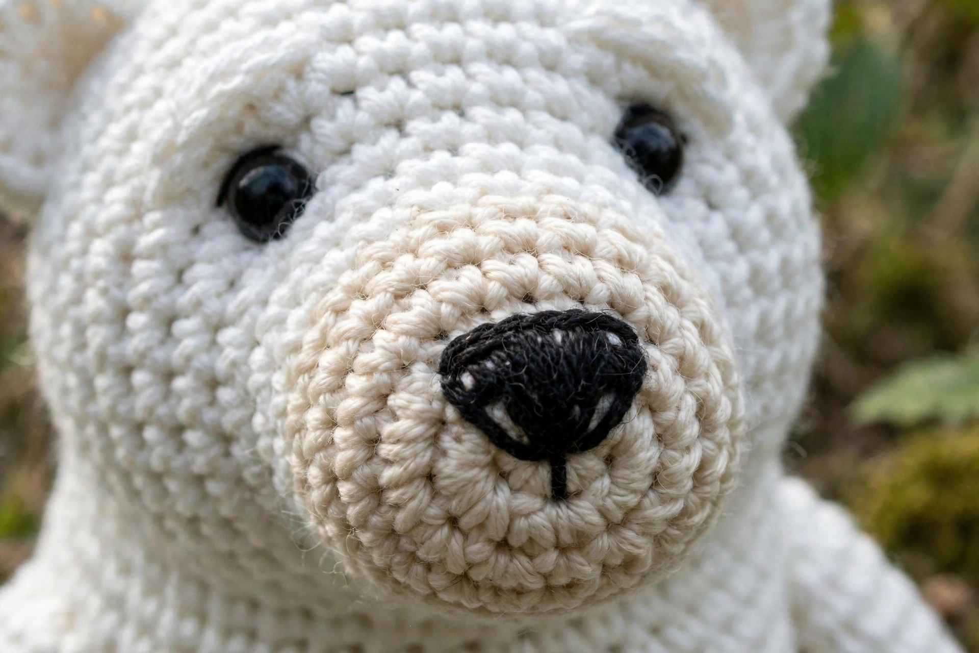 Close-up of a white crocheted polar bear face showing the cream muzzle, embroidered black nose and dark safety eyes